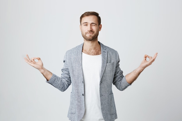 Handsome guy trying meditate, peeking during yoga session