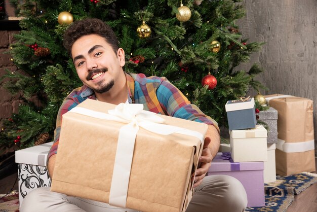 Красивый парень пытается открыть самую большую подарочную коробку.
