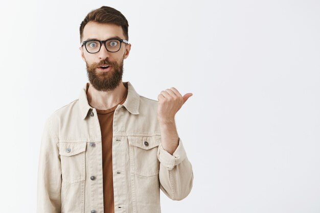 Handsome happy bearded man in glasses posing against the white wall