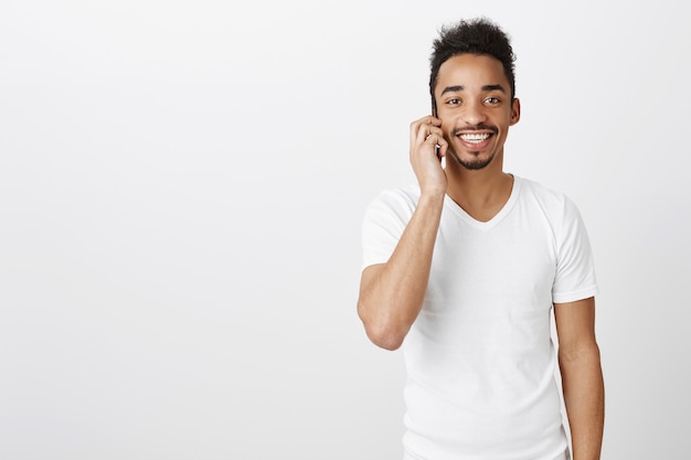 ハンサムな幸せな黒人男性の笑顔と携帯電話で話しています。