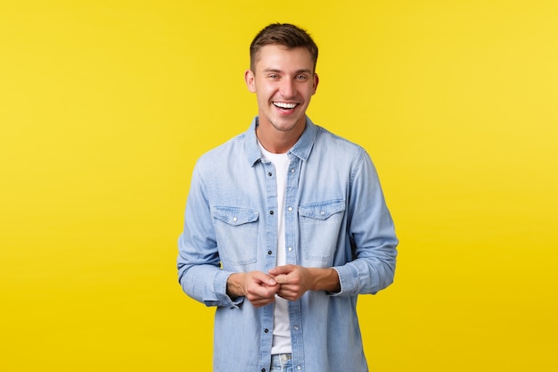 Handsome happy male student in casual outfit, laughing and smiling, having lively conversation. Man looking joyfully camera, standing yellow background, talking to friend.