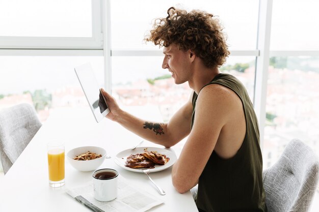 タブレットを使用しながらキッチンに座っているハンサムな幸せな男