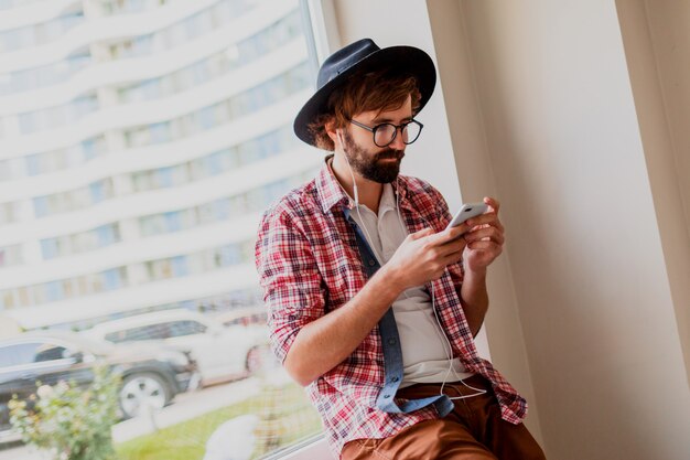 Красивый хипстерский мужчина с бородой в солнцезащитных очках, отправляющий SMS-сообщения через смартфон и ведущий блог в социальных сетях