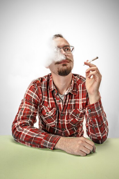 Handsome hipster man smoking cigarette at home. Man looking upwards and enjoying spending free time.