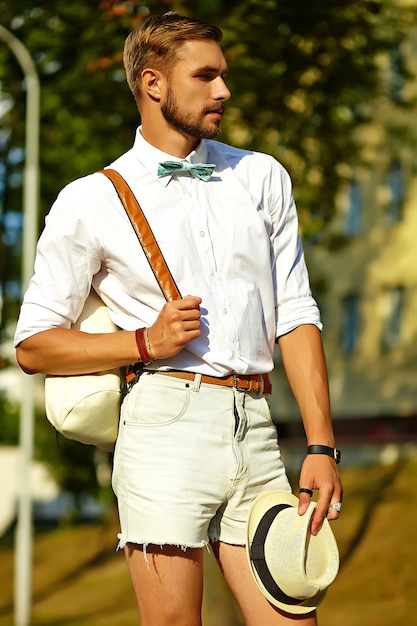 Uomo di modello bello hipster in abiti estivi alla moda in posa in cappello con borsa