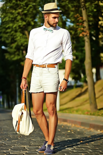 Красивый битник модель мужчина в стильной летней одежде позирует в шляпе с сумкой