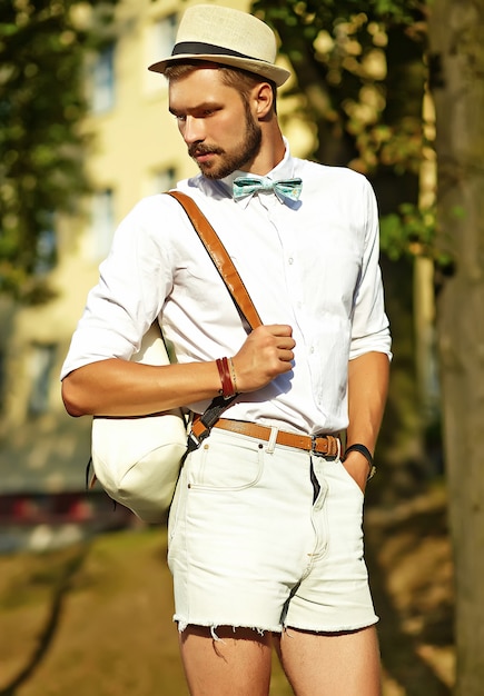 Uomo di modello bello hipster in abiti estivi alla moda in posa in cappello con borsa