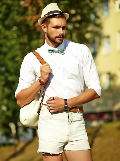 Uomo di modello bello hipster in abiti estivi alla moda in posa in cappello con borsa