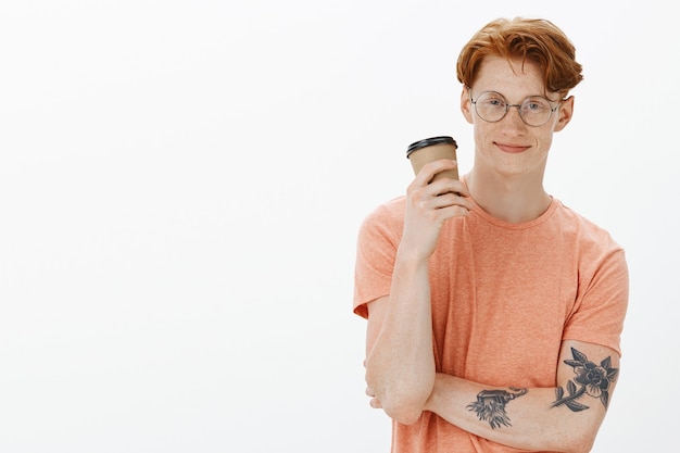 Free photo handsome hipster redhead man in glasses drinking coffee and smiling casually