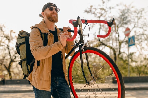 Handsome hipster stylish bearded man in jacket and sunglasses walking alone in street with backpack on bicycle healthy active lifestyle traveler backpacker