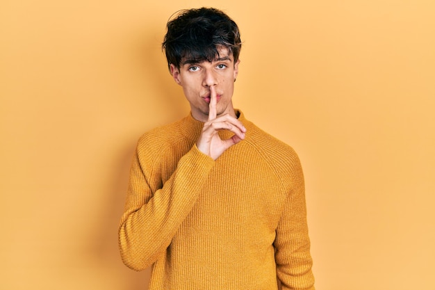 무료 사진 캐주얼한 노란 스웨터를 입은 잘생긴 스터 젊은이가 입술에 손가락을 고 조용히 하라고 요청합니다. 침과 비밀 개념