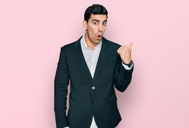 Free photo handsome hispanic man wearing business clothes surprised pointing with hand finger to the side open mouth amazed expression