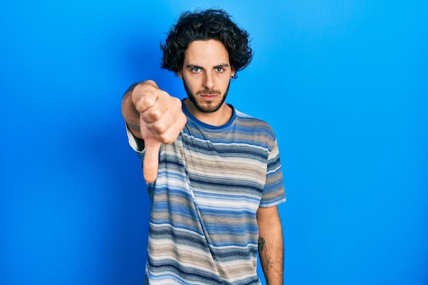 Handsome hispanic man wearing casual clothes over pink background looking unhappy and angry showing rejection and negative with thumbs down gesture. bad expression.