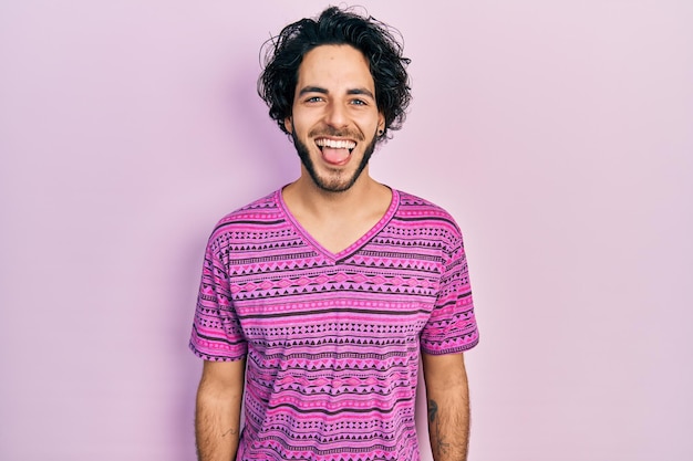 Free photo handsome hispanic man wearing casual pink t shirt sticking tongue out happy with funny expression emotion concept