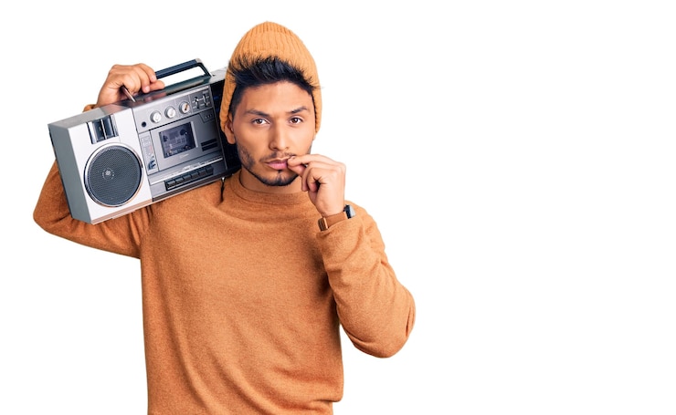 Free Photo handsome latin american young man holding boombox listening to music mouth and lips shut as zip with fingers secret and silent taboo talking