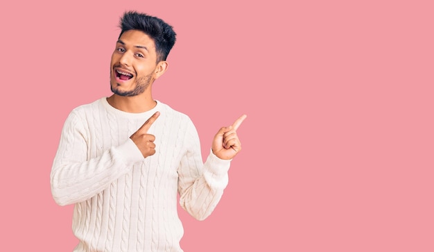 Free photo handsome latin american young man wearing casual winter sweater smiling and looking at the camera pointing with two hands and fingers to the side