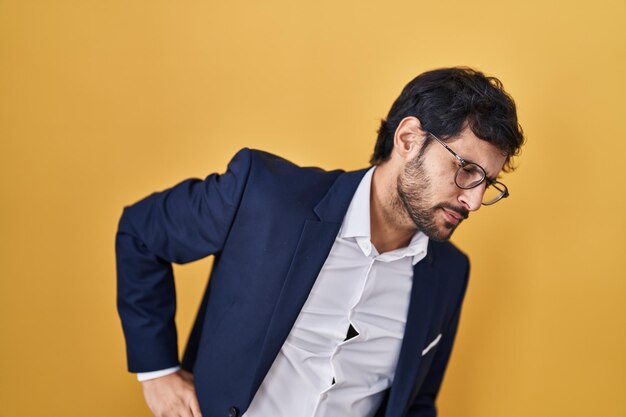 Handsome latin man standing over yellow background suffering of backache touching back with hand muscular pain