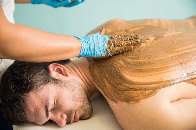 Foto gratuita bel giovane latino che riceve un massaggio e un bagno di fango durante la sua visita a una spa