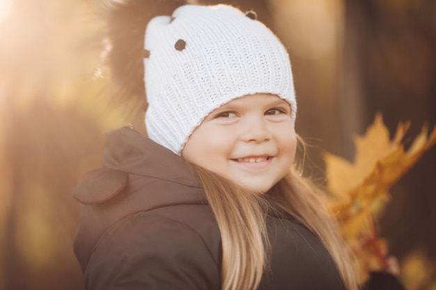 Handsome little girl with long chestnut hair and pretty smile in black jacket goes for a walk in the park in autumn