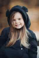 Foto gratuita una bella bambina con lunghi capelli castani e un bel sorriso in giacca nera va a fare una passeggiata nel parco in autunno