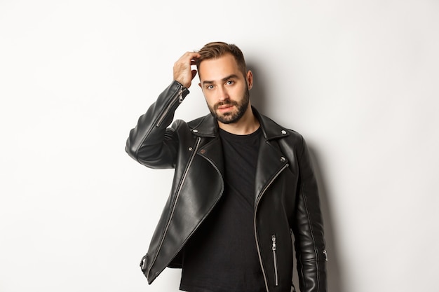 Handsome macho man in black biker jacket, touching his haircut and looking cool