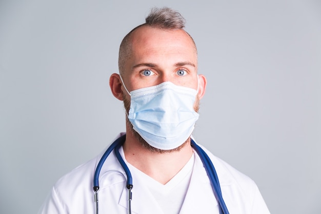 Handsome male doctor on gray wall with protective medical mask on face