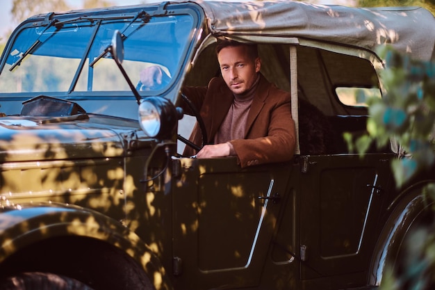 Handsome male elegantly dressed sit in the retro military machine.