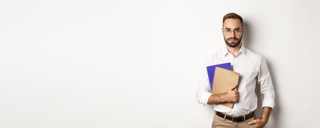 Free photo handsome male employee holding notebooks looking confident standing over white background