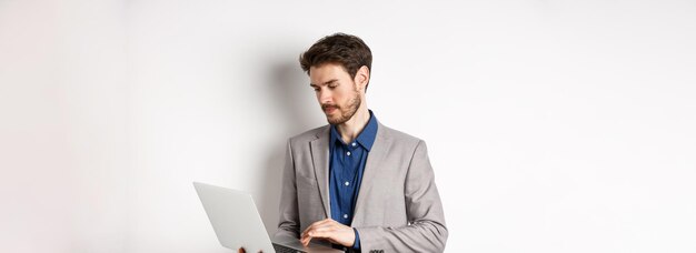 Красивый мужчина-предприниматель, работающий на ноутбуке, серьезно смотрит на экран, стоящий на белом фоне