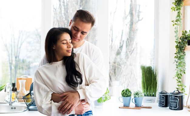 Handsome male hugging ethnic girlfriend with closed eyes