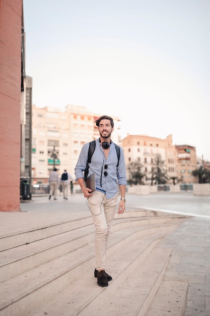 Handsome male tourist with laptop walking down staircase