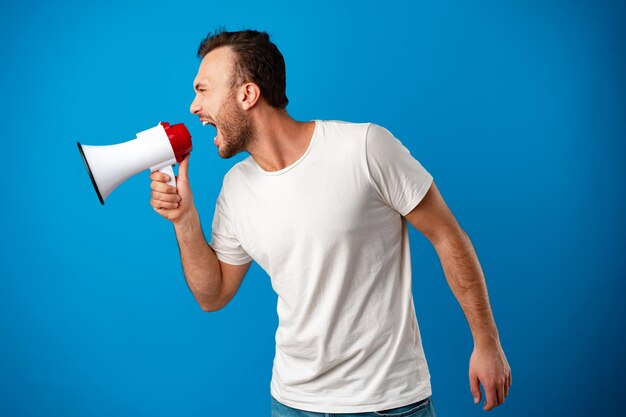 handsome man over blue wall shouting through a megaphone