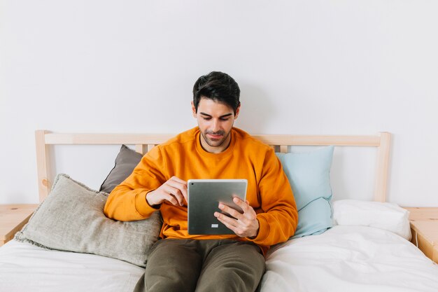 Handsome man browsing tablet on bed