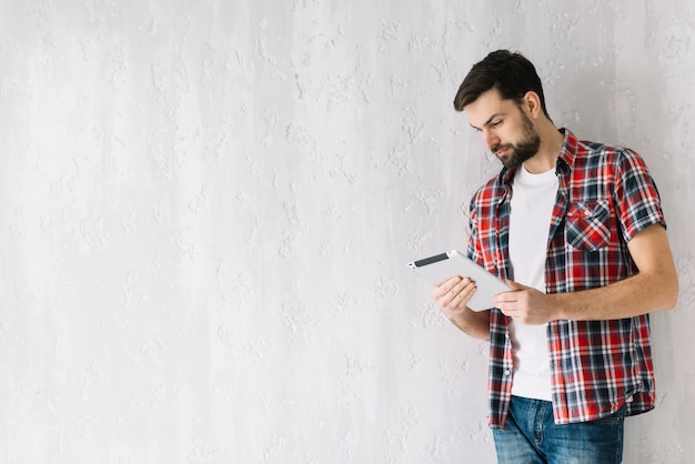 Free photo handsome man browsing tablet near wall