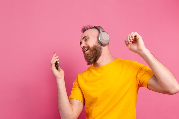 ピンクの背景に分離された携帯電話とヘッドフォンでカジュアルダンスのハンサムな男