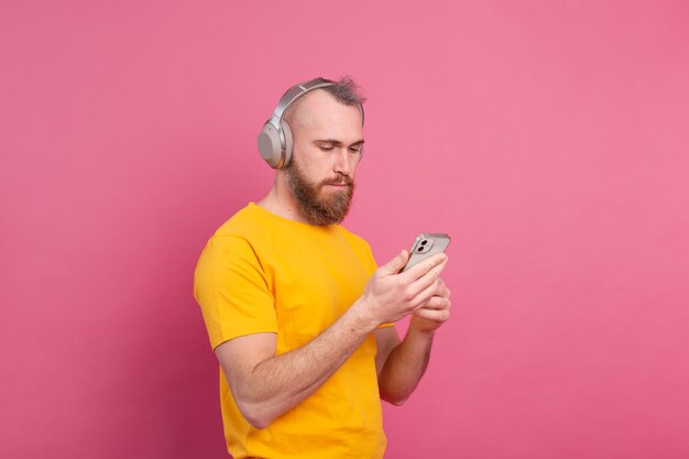 Handsome man in casual listening to music with headphones isolated on pink background