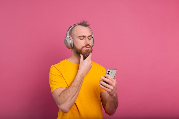 Красивый мужчина в непринужденной обстановке слушает музыку в наушниках, изолированных на розовом фоне
