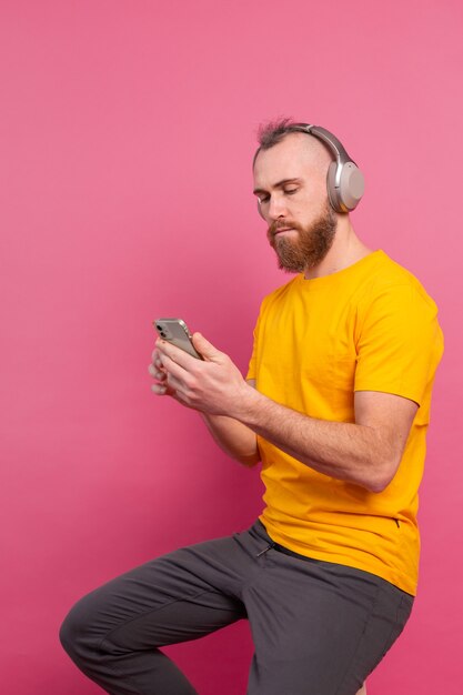 Handsome man in casual listening to music with headphones isolated on pink background