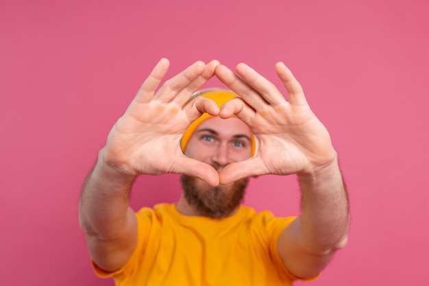 Handsome man in casual listening to music with headphones isolated on pink background