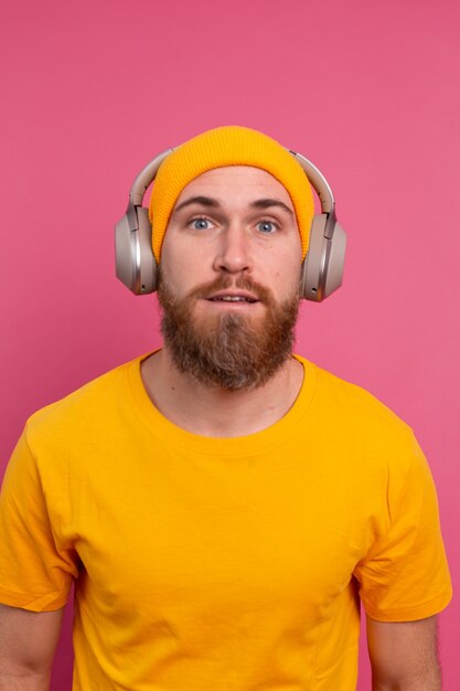 Handsome man in casual listening to music with headphones isolated on pink background