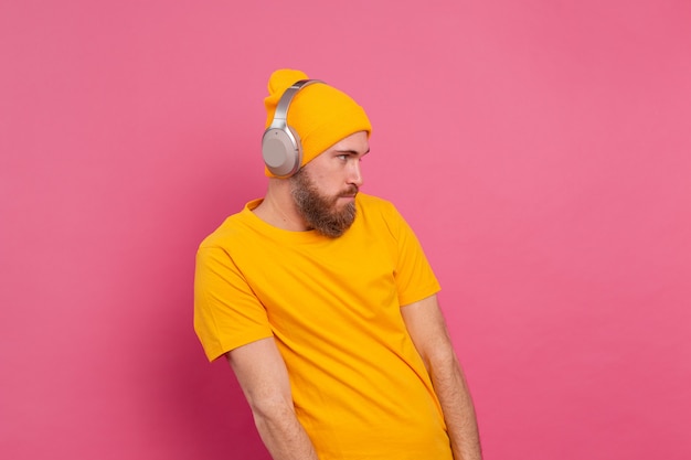 Handsome man in casual listening to music with headphones isolated on pink background