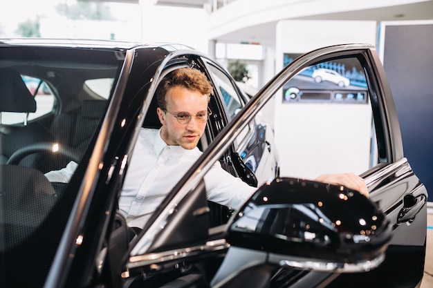 Handsome man choosing a car in a show room