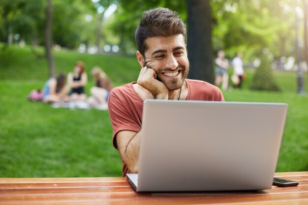 ハンサムな男はラップトップで公園のwifiとビデオ通話の友人を接続します