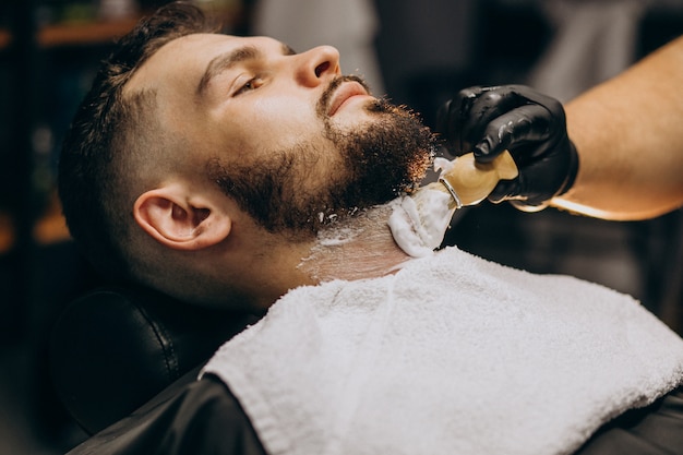 Free photo handsome man cutting beard at a barber salon