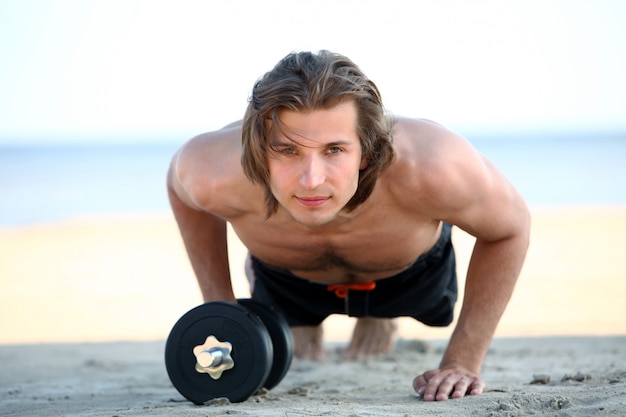 Handsome man doing fitness exercises on the beach