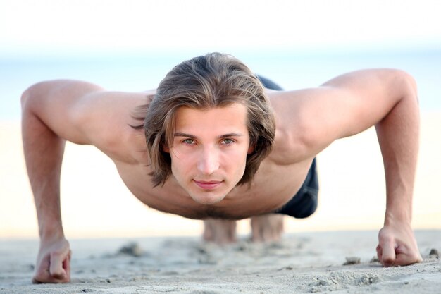 Handsome man doing push ups on the beach