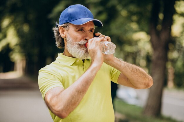 Handsome man drinking water in park after jogging