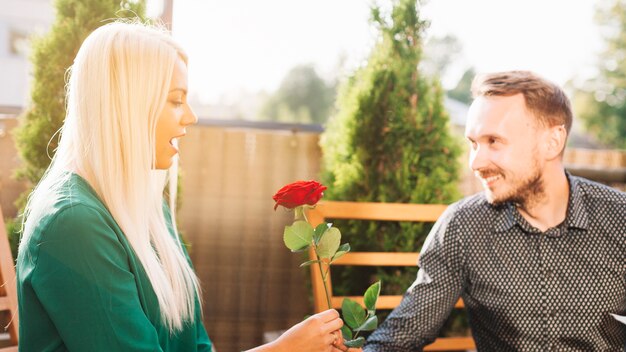 Handsome man giving red rose to surprised blonde young woman