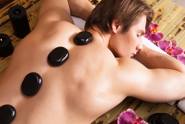 Handsome man having stone massage in spa salon. Healthy lifestyle.