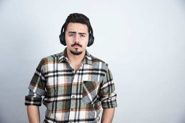 handsome man in headphones looking to camera over white wall.